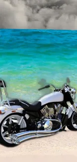 Motorcycle parked on a sandy beach with turquoise sea and cloudy sky.