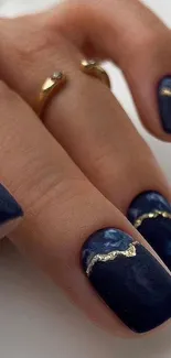 Close-up of a hand with navy blue nails and gold accents in artistic design.