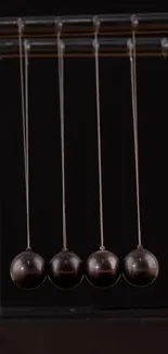 Newton's cradle with four black spheres on a black background.