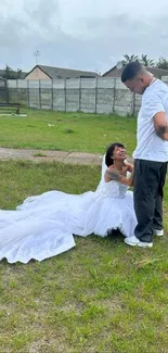 Bride kneeling outdoors beside groom on grassy field.