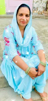 Lady in light blue traditional attire sitting outdoors.