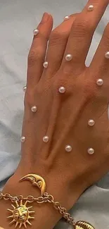 Hand with pearls and golden bracelet on soft fabric.