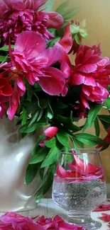 Vibrant pink peonies in a vase with a glass.