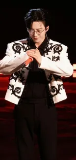 Performer in black and white jacket on a red stage.