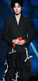 Stylish performer holding a red microphone on stage in elegant attire.