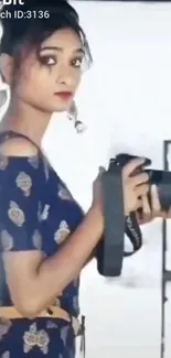 Elegant photographer in blue dress holds camera with poised expression.