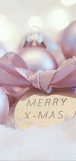 Pink Christmas baubles in snow with festive ribbon.