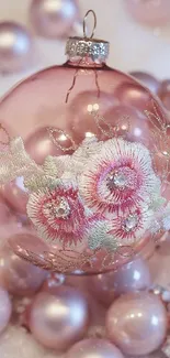 Pink Christmas ornament with floral embroidery in soft hues on a phone wallpaper.