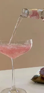 Pink beverage being poured into a glass with donut on side.