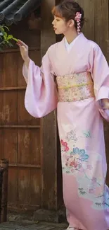 Woman in a pink kimono stands gracefully in a traditional setting.