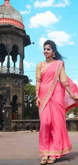 Woman in a pink saree with historic backdrop.