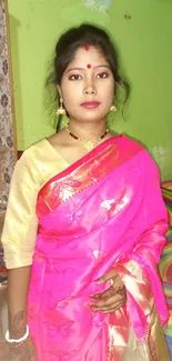 Woman in a vibrant pink saree with a colorful room and elegant demeanor.