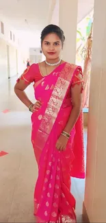 Woman in a vibrant pink saree standing in a hallway.