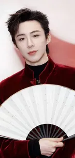 Stylish person in a red coat holding a white fan against a modern backdrop.