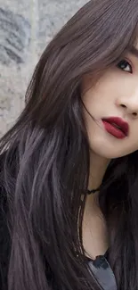 Portrait of a model with dark hair and red lips against a stone background.