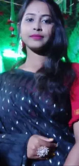 Woman in black saree at festive event with green and gold decor.