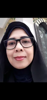 Portrait of woman in glasses and headscarf against architectural backdrop.