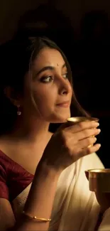 Portrait of woman in traditional attire holding a cup with warm light.