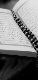 Open Quran on a stand with prayer beads in black and white.