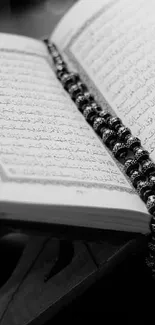 Black and white wallpaper of Quran on a wooden stand with prayer beads.