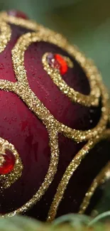 Close-up of a red ornament with gold glitter details on green background.