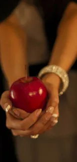 Elegant hands holding a red apple against a dark background.