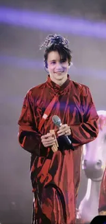 Performer in elegant red attire on stage with dark background.