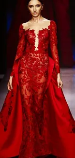 Model in an elegant red lace gown on a runway, showcasing fashion sophistication.