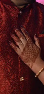 Intricate mehndi design on hand with red fabric background.