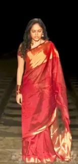 Woman in red saree on railway tracks at night.