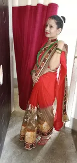 Woman in red saree standing by doorway with vibrant design.