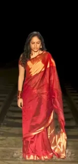 Woman in a vibrant red saree on railway tracks.