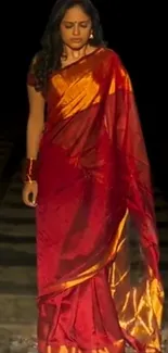 Woman in a red sari standing on train tracks with a dark background.