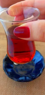 Red tea in glass cup with hand, on rustic table.