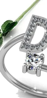 Sparkling ring with letter 'D' and red rose on white background.