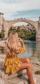 Woman in yellow dress by scenic river bridge.