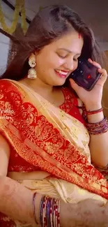 Woman in red saree talking on phone, smiling elegantly.