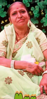 A woman in a pastel green saree with floral design and lush green leaves.