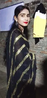 Woman wearing a black saree with gold stripes poses elegantly.