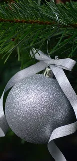 Silver Christmas ornament hanging on green pine branches, shimmering in light.