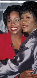 Two women smiling and embracing in stylish outfits.