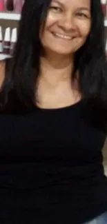 Smiling woman in black top with nail polish backdrop.