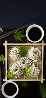 Soba noodles on bamboo mat with green leaves and chopsticks.