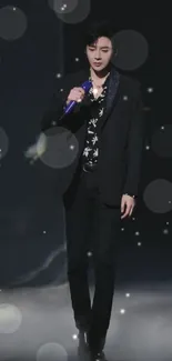 Elegant performer in black suit with blue microphone on stage.