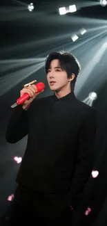 Performer holding a red microphone on stage under dramatic lighting.