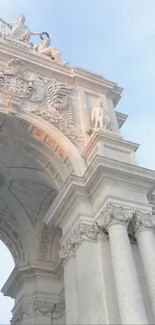 Elegant stone archway with classical sculptures against a light blue sky.