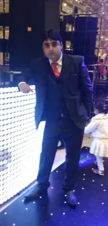 Man in suit standing by LED wall with child at an event.