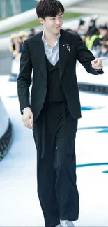 Man in a stylish black suit walking confidently in an urban environment.