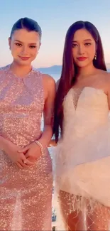 Two women in elegant dresses at sunset beach.