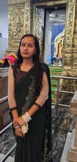 Woman in traditional green sari inside ornate temple.